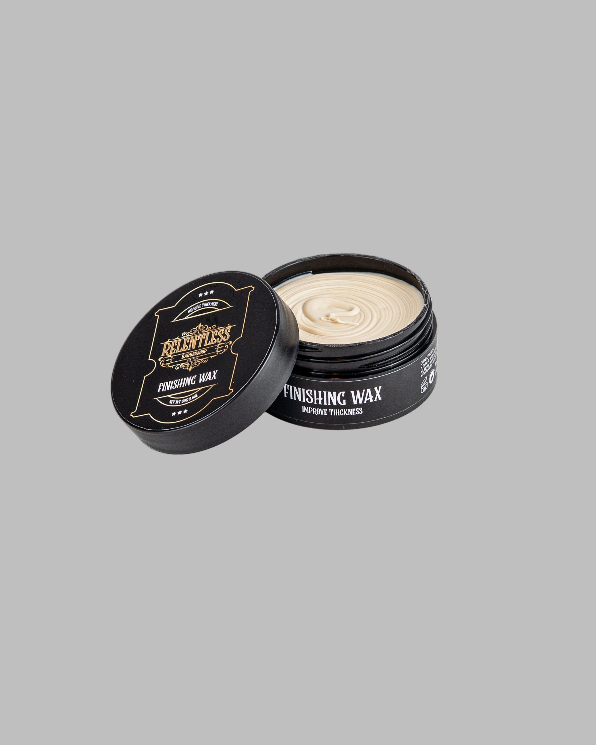 Black container of finishing wax with open lid on a white background